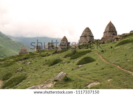 city of the dead in Kabardino-Balkaria, stone houses burial on the background of green mountains and hills, narrow paths along the slope, bushes near the buildings, cemetery