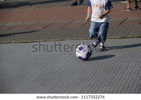 Little boy playing soccer on the street.