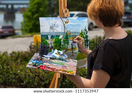 Artist; young woman paints on a canvas an urban landscape of a summer of oil paints in city park