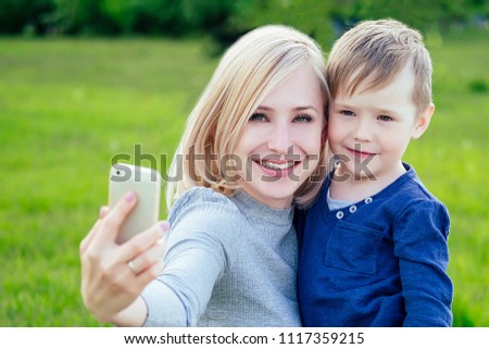 attractive mother and loved son take pictures selfie on phone in the park on a background of green grass and trees