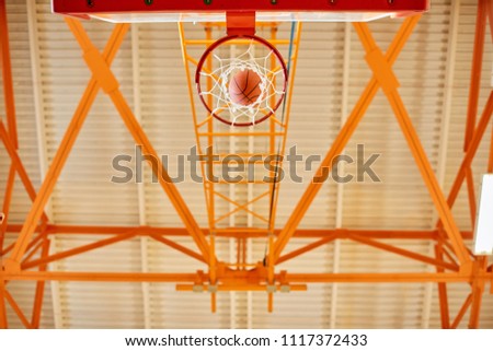 From below shot of basketball ball falling on ground through basket in gym. 