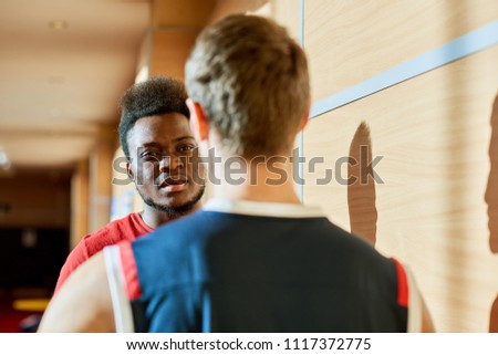Two sportsmen in basketball uniform standing in gym and talking with each other before match. 