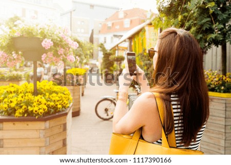 Woman on city tour taking picture of beautiful cafe flowers with her smartphone