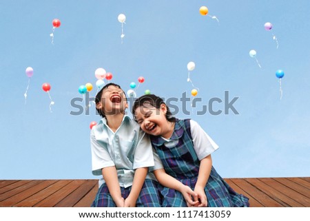 Funny Asian little kids brother and sister sitting on the wooden terrace with colourful balloons background.laughing and Happiness of cute kid in uniform school,Education,Family,Children Concept. Royalty-Free Stock Photo #1117413059