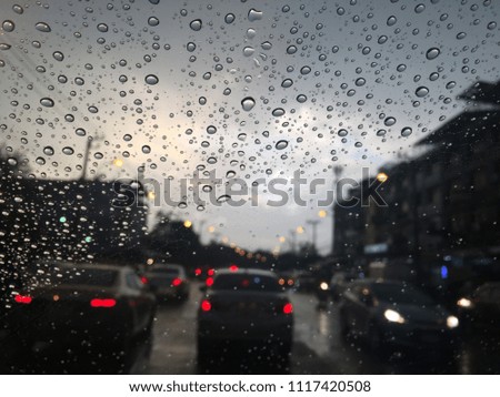 Raindrops on the windshield, traffic in the city on a rainy day at evening. Car windshield view, colorful bokeh, blurred and dark background.