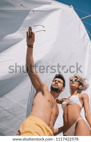 low angle view of shirtless man in swimwear pointing by hand to girlfriend on yacht 