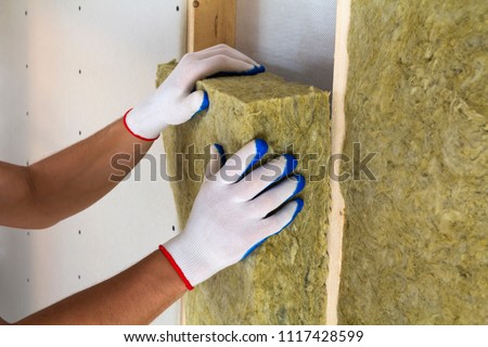 Close-up of worker hands in white gloves insulating rock wool insulation staff in wooden frame for future walls for cold barrier. Comfortable warm home, economy, construction and renovation concept. Royalty-Free Stock Photo #1117428599