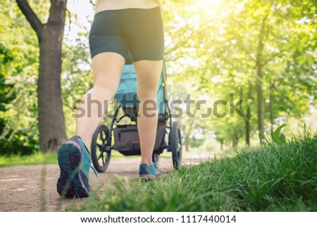 Walking woman with baby stroller enjoying summer day in park. Jogging or power walking supermom, active family with baby jogger. Royalty-Free Stock Photo #1117440014