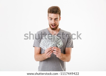 Image of excited shocked young man standing isolated over white wall background holding money.