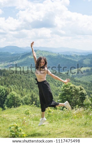 Cute girl is jumping against the backdrop of mountains and forests. Sunny summer day