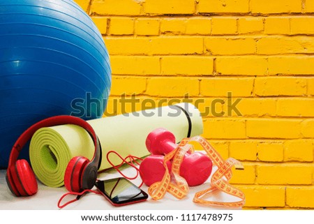 dumbbells, Mat, smartphone and earphones on yellow brick wall background