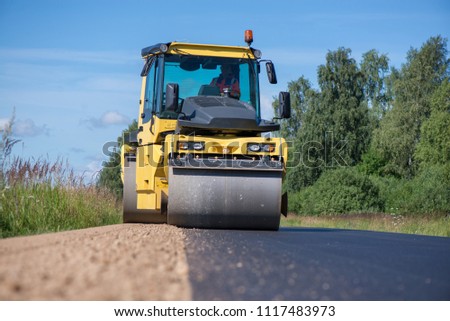 
Yellow heavy vibration roller at asphalt pavement works. Road repairing in city. Road construction workers repairing highway road on sunny summer day. Heavy machinery, loaders and trucks