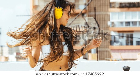 Energy woman with yellow headphones listening to music on the exterior terrace  wears white T-shirt, shorts. Long hair in tail is flying overhead from jump.