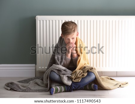 Sad little boy suffering from cold on floor near radiator Royalty-Free Stock Photo #1117490543