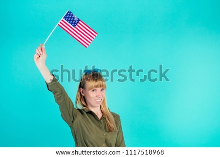 young and active blonde woman holds American flag in studio on blue background