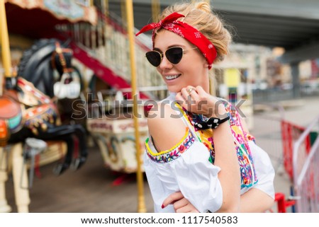 Portrait Of Beautiful happy hipster woman posing on background of street attractions. Closeup of smiling female model sith sealthy skin showing happy smile. Eyecare. High Resolution Image