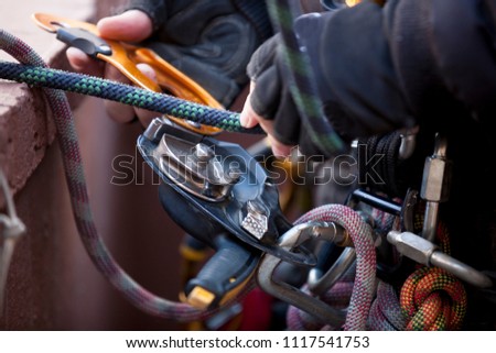 Top view picture of industrial rope access worker hand connecting Nylon low stretch 
rope into descender which its attached with harness loop working at height abseiling rope blurry back ground 