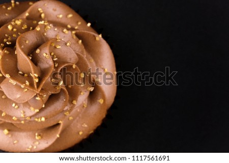 Cupcake with whipped chocolate cream, decorated gold confectionery sprinkling on black background. Picture for a menu or a confectionery catalog. Top view. Close up.