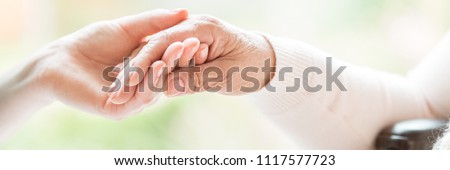 Close-up of tender gesture between two generations. Young woman holding hands with a senior lady. Blurred background. Panorama. Royalty-Free Stock Photo #1117577723
