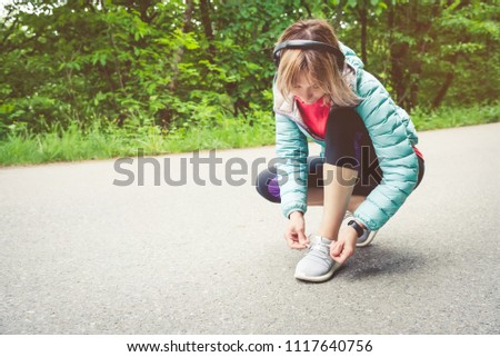 Portrait of a sporty blonde girl in headphones on a run in the forest. A girl sitting tied shoelaces on cross-country shoes. Active lifestyle. Sport