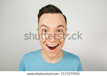 Close up portrait of young happy smiling guy, dressed in a blue t-shirt on a light background.