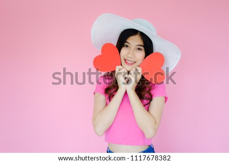 Portrait beautiful asian woman on pink background, happy valentine day in love concept, model holding red heart sign in hand with hat
