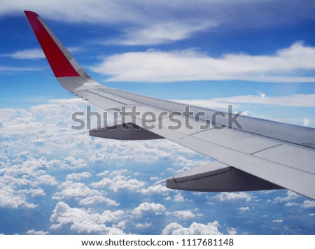 crop view of a white silver metallic airplane wing from passenger window as the machine flying high under bright blue sky on a cloudy day