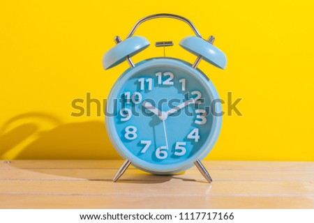 Blue analog alarm clock on the wooden table over yellow background.Alarm clock showing time 10 o'clock.