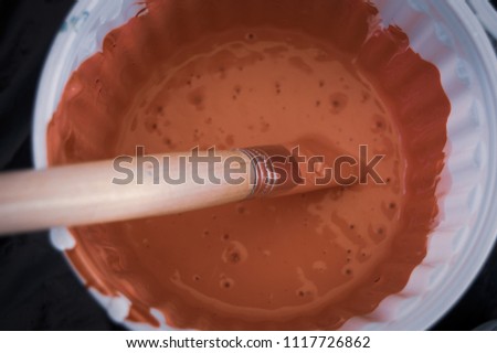 Top close up photograph of a white container filled with soft orange paint and a large paintbrush background 