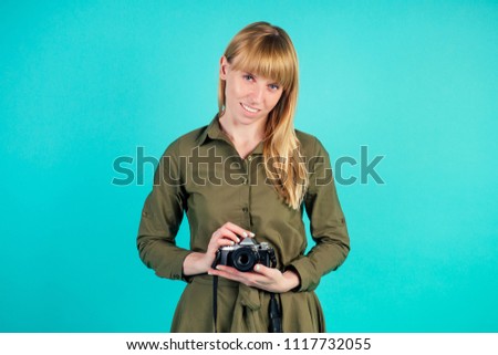 blonde woman holds a small camera in studio on blue background