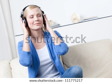 Sitting on the sofa beautiful woman in headphones listens to music
