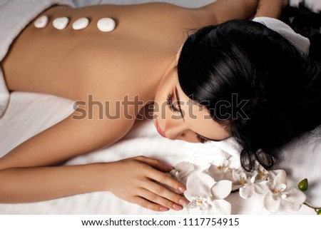 Relaxed beautiful young woman with stones on her back in spa salon. Beauty treatment