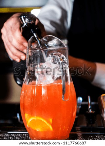The barman pours soda water from a siphon into a jug with a soft fruit drink
