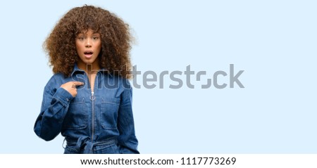 African american woman wearing blue jumpsuit happy and surprised cheering expressing wow gesture, pointing with finger