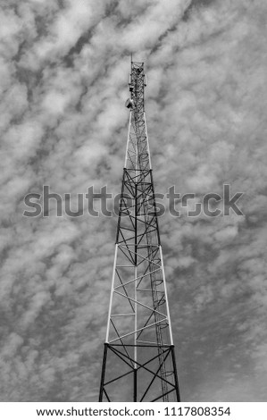 Telecommunications mobile tower in the middle of the image with a sky and an interesting white cloud background.