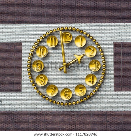 Gold watch with numbers in on plates on a brick wall