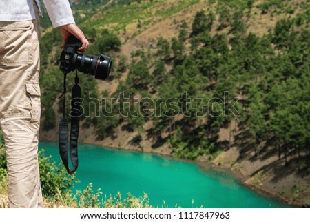 Photographer holding camera in front of beautiful lake in mountains