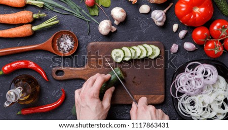 Image on top of fresh vegetables, mushrooms, cutting board, oil, knife, hands of cook on table