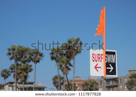 A bright orange flag divides a California beach into surf zone and swim zone. Copy space over blue sky.