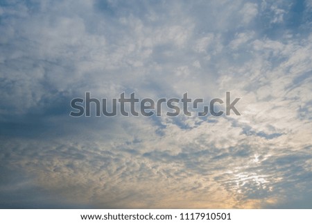 Skyscape of early morning cirrus and cumulus clouds with a ray of sunshine at bottom of frame. 