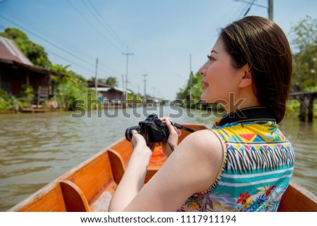 Woman traveler sitting on the boat and taking photo view of river and building by camera on Damnoen Saduak floating market.