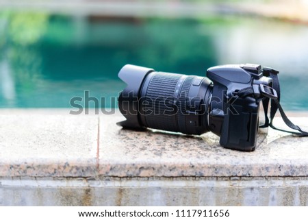 Black DSLR camera put on the edge of the swimming pool.