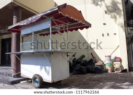 Abandoned food cart chained to an abandoned building. To the side, black trash bags and empty containers.