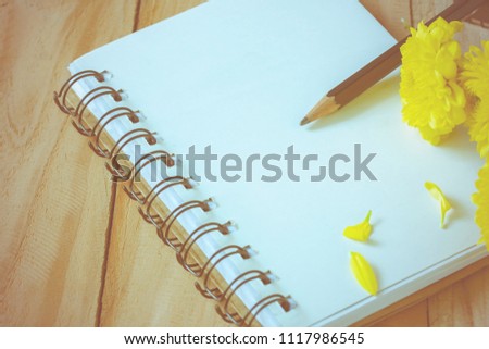soft focus photo of pencil and notebook on wooden floor with yellow flower, vintage tone