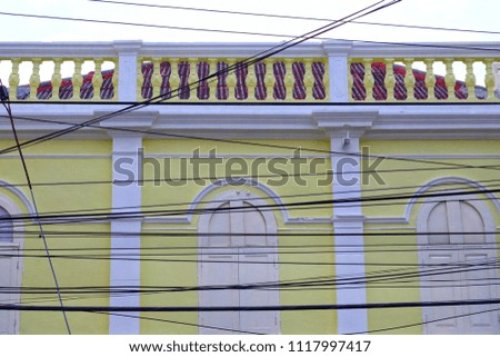 Messy electricity cables with white yellow wall of a building and rooftop