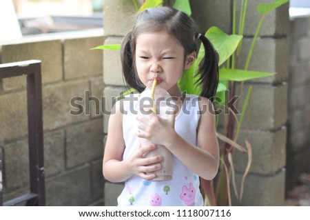 Little girl drinking chocolate milk out of a plastic glass with a straw.