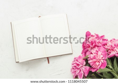 Pink peonies and an open diary on a light stone background. Flat lay, top view.