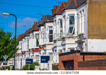 A row of typical British terraced houses around Kensal Rise in London with estate agent boards
