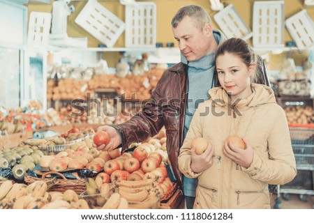 Happy little girl with her loving father buying fresh apples in fruit store