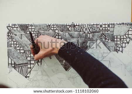 Male hand of artist is drawing with ink pen, monochrome picture of houses, copy space